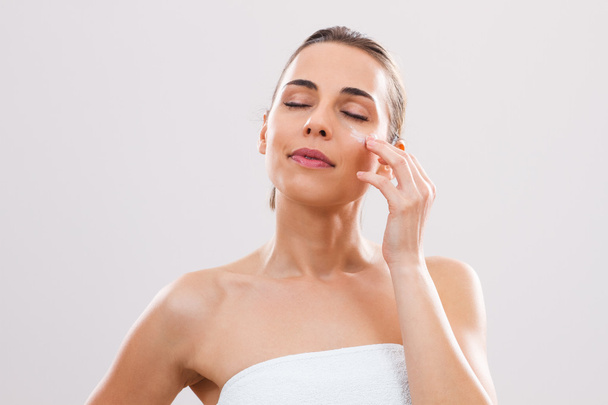 Woman is applying lotion on her face - Φωτογραφία, εικόνα