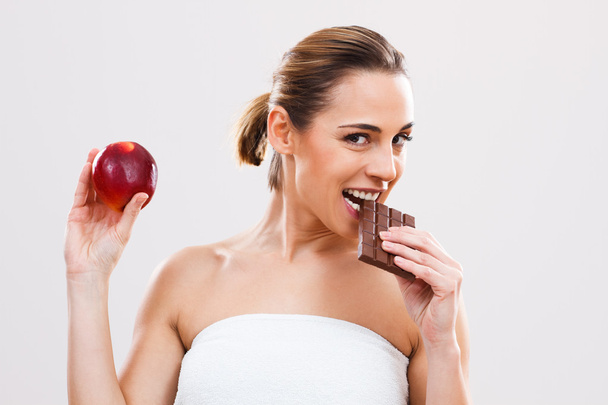 Woman biting chocolate and holding apple - Fotó, kép