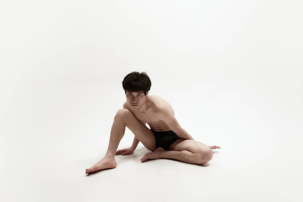 Studio image of young handsome asian man posing shirtless in underwear on floor with attentive look against white background. Concept of male body aesthetics, style, fashion, health, mens beauty - Foto, Imagem