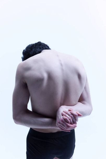 Round back, healthy spine. Young guy posing shirtless, holding hands behind back against white studio background. Relief male body. Male body aesthetics, style, fashion, health, mens beauty concept - 写真・画像