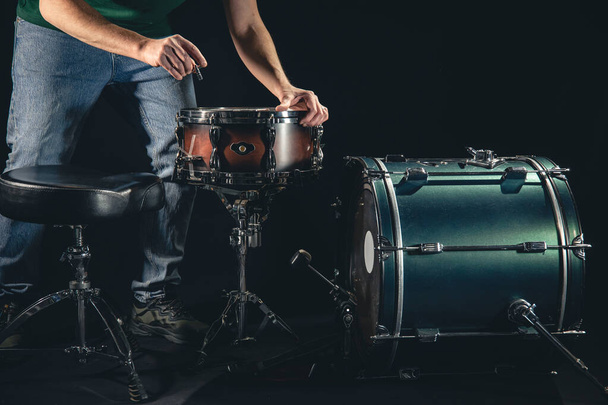 Um baterista masculino e um kit de bateria em um fundo preto, o músico está se preparando para tocar. - Foto, Imagem