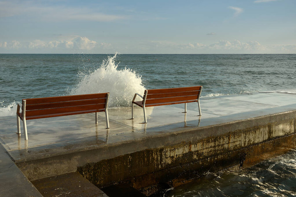Waves flow over the promenade with two benches. - Fotografie, Obrázek