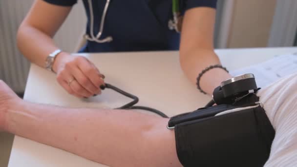 A beteg vérnyomását mérő orvos közeli képe. látni a betegek betegségének lefolyását az orvosi rendelőben. Modern orvosi ellátás otthon - Felvétel, videó