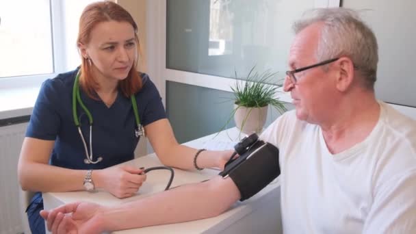 Терапевт измеряет кровяное давление пациента мужского пола. Кровяное давление и проблемы с сердцем у пожилого человека. Высококачественное 4k видео - Кадры, видео
