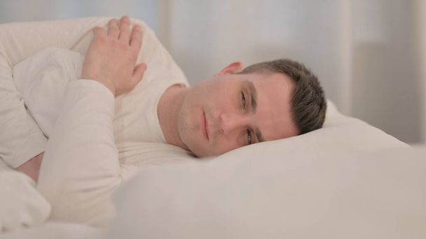 Pensive Mladý muž spí v posteli na boku - Fotografie, Obrázek