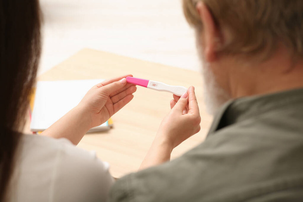 Daughter showing her father pregnancy test indoors, closeup. Grandparents' reaction to future grandson - 写真・画像