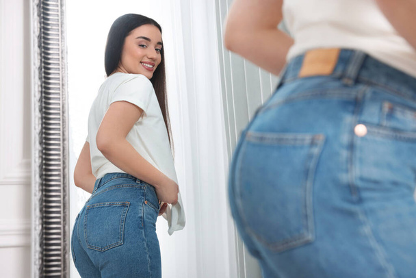 Young woman in stylish jeans near mirror indoors - Foto, Imagen