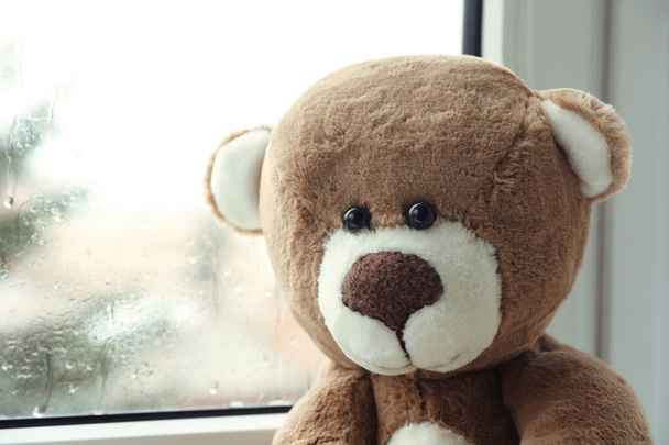 Cute lonely teddy bear on windowsill indoors, closeup - Фото, изображение