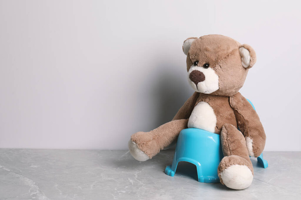 Teddy bear on baby potty near light wall, space for text. Toilet training - Zdjęcie, obraz