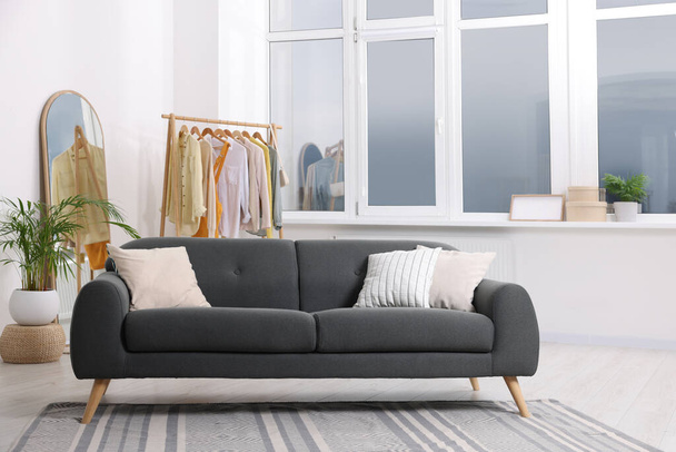 Stylish living room interior with comfortable grey sofa and clothing rack - Foto, afbeelding