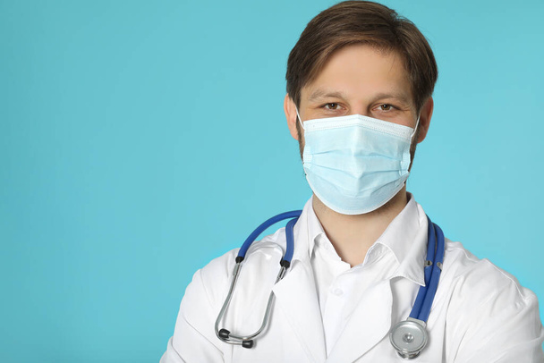 Doctor or medical assistant (male nurse) with protective mask and stethoscope on turquoise background - Fotó, kép