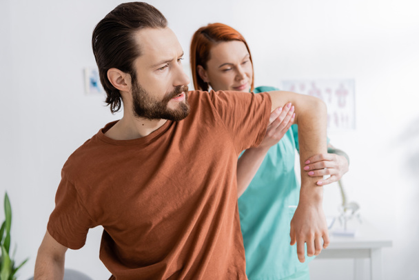 chiropractor flexing injured arm of bearded patient in consulting room - Foto, Imagen