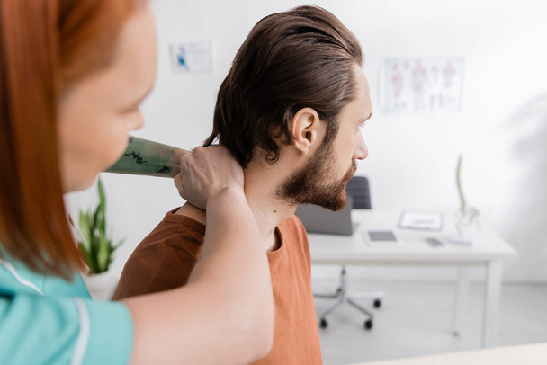 fisioterapeuta borrosa examinar el cuello del hombre lesionado durante la cita en el centro de rehabilitación - Foto, Imagen