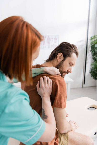 blurred chiropractor examining painful shoulder of injured man in consulting room - Valokuva, kuva