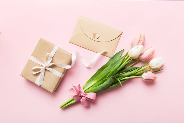 Pink tulips flowers and gift or present box on colored table background. Mothers Day, Birthday, Womens Day, celebration concept. Space for text top view. - Photo, Image