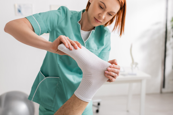 Rotschopf manueller Therapeut massiert Füße verletzter Patientin in Reha-Zentrum - Foto, Bild