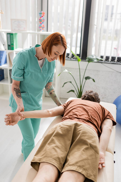 fizjoterapeuta zginający ramię mężczyzny podczas wykonywania masażu przeciwbólowego w gabinecie konsultacyjnym - Zdjęcie, obraz