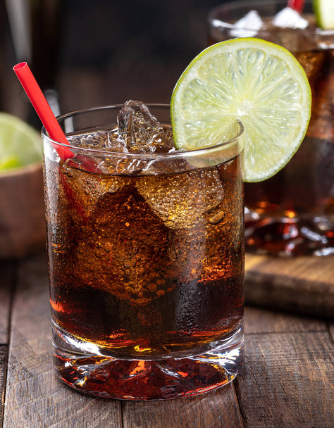 Rum and cola cocktail with lime slice on rustic wooden table.  Closeup - Φωτογραφία, εικόνα