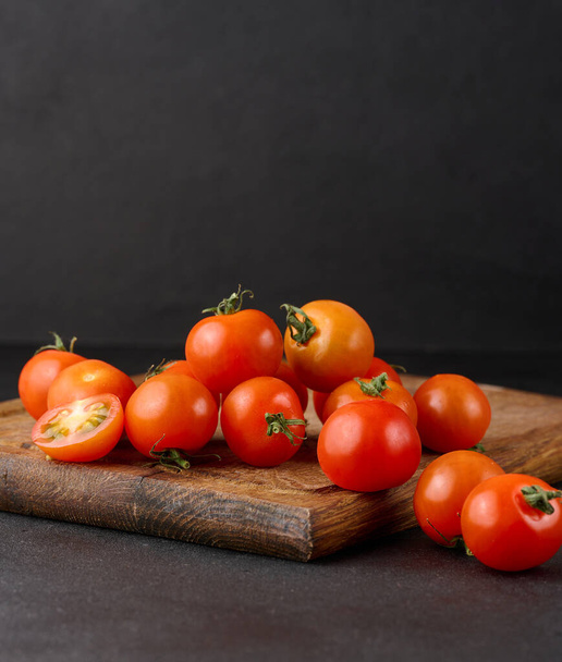 Bouquet de tomates cerises rouges mûres sur une planche en bois, fond noir - Photo, image