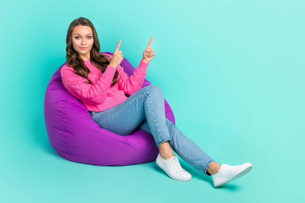 Full length photo of confident shiny girl wear sweater showing fingers empty space sitting bean bag isolated turquoise color background. - Fotó, kép