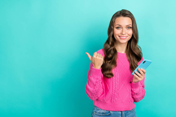 Photo of adorable woman wavy hairdo dressed knitwear sweater directing empty space hold smartphone isolated on teal color background. - Foto, Imagen