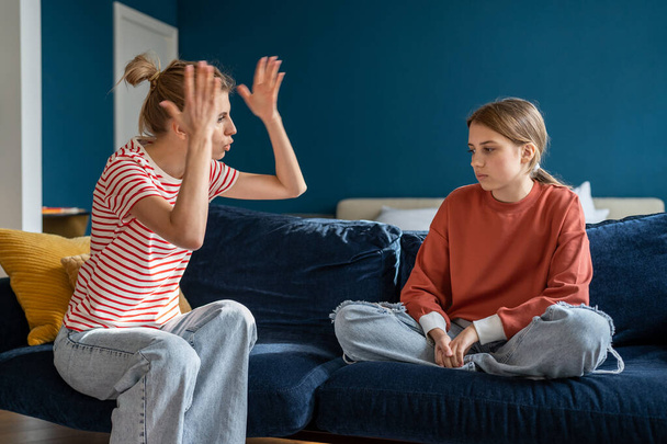 Junge wütende emotionale Mutter schreit beunruhigte Teenager-Tochter an, wütende Eltern-Mutter, die sich mit jugendlichen Verhaltensproblemen beschäftigt, schreit aufgebrachte Jugendliche an, während sie zu Hause auf dem Sofa zusammensitzt - Foto, Bild