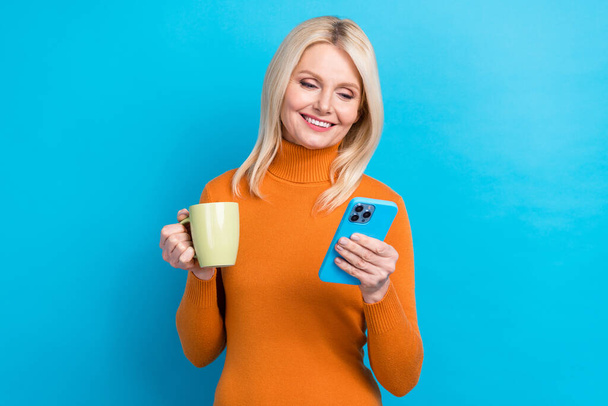 Photo of good mood blogger reading fresh news pensioner hold phone enjoy tradition drink cappuccino isolated on aquamarine color background. - Fotó, kép