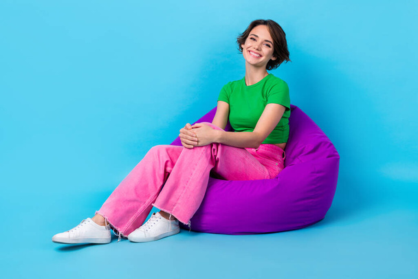 Full length photo of funny cute lady wear green t-shirt relaxing bean bag empty space isolated blue color background. - Fotó, kép