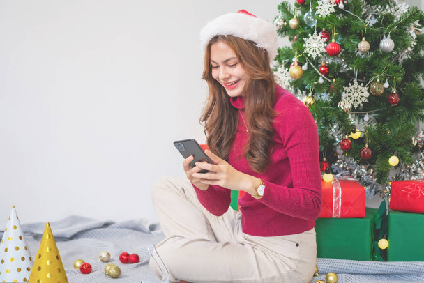 Καλά Χριστούγεννα και καλές γιορτές! Μια νεαρή γυναίκα με ένα όμορφο πρόσωπο σε ένα κόκκινο πουκάμισο δείχνει χαρά με κουτιά δώρων σε ένα σπίτι με ένα χριστουγεννιάτικο δέντρο διακοσμημένο με ένα χριστουγεννιάτικο δέντρο. Πορτρέτο πριν τα Χριστούγεννα - Φωτογραφία, εικόνα