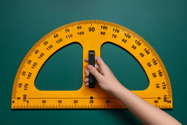 Woman holding protractor with measuring length and degrees markings near green board, closeup - Foto, immagini
