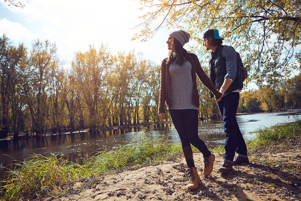 Hand in hand along the riverbank. Full length shot of an affectionate young couple spending a day in nature - 写真・画像
