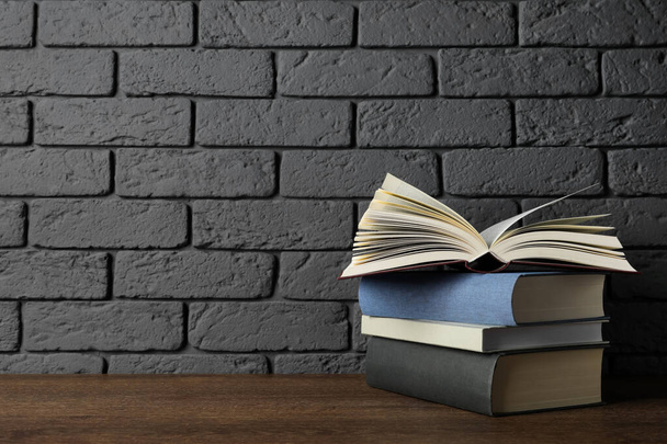 Stack of hardcover books on wooden table near dark brick wall, space for text - Foto, imagen