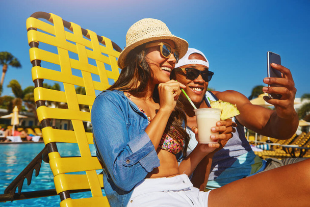 Selfie del sorriso estivo. una giovane coppia affettuosa che si fa dei selfie mentre si gode qualche drink a bordo piscina - Foto, immagini