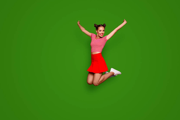 Full-length full-size view of jumping laughing and happy woman dressed in colourful bright clothes isolated on red background. - Fotó, kép