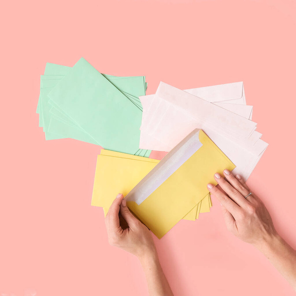 Colored paper envelopes hold human hands on a pink background. Top view. Place for text and logo. The concept of packaging, stationery, holidays, gifts. High quality photo - Foto, immagini