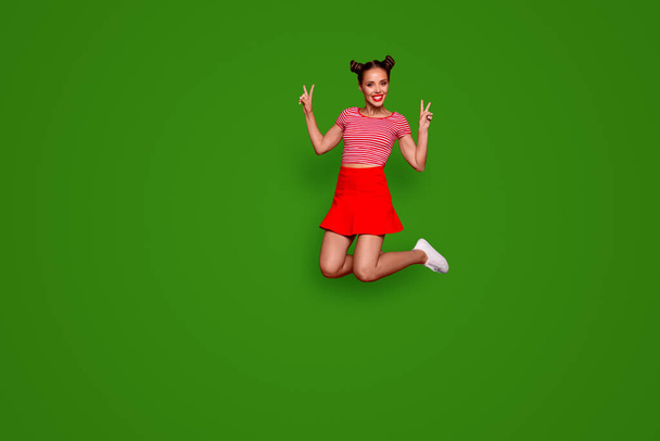 Full-length full-size view of jumping laughing and pretty woman dressed in colourful bright clothes shows a v-sign isolated on red background. Joy fun concept. - Zdjęcie, obraz