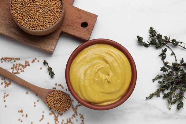 Bowl with delicious mustard, seeds and dry thyme on white marble table, flat lay - Foto, Bild