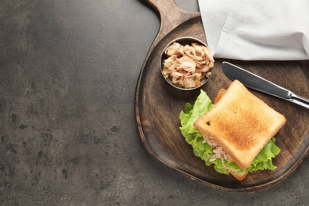 Delizioso panino con tonno, foglie di lattuga e coltello sul tavolo grigio, vista dall'alto. Spazio per testo - Foto, immagini