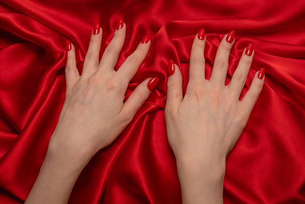 Une main de femme avec des ongles rouges essaie d'arracher le tissu de soie rouge.  - Photo, image