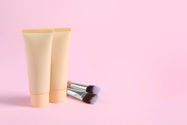 Tubes of skin foundation and brushes on pink background, space for text. Makeup product - Foto, immagini