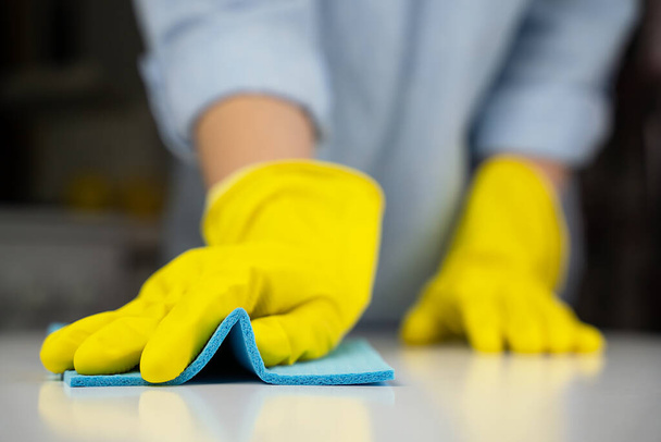 黄色のゴム手袋の主婦は、ラグでキッチンテーブルを拭く。家事の概念。接近中だ。選択的焦点. - 写真・画像