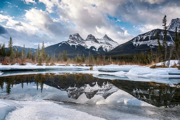 Hermosa vista de las montañas Three Sisters con nieve cubierta en el reflejo del río arco congelado en la mañana del invierno en Canmore, Alberta, Canadá - Foto, imagen