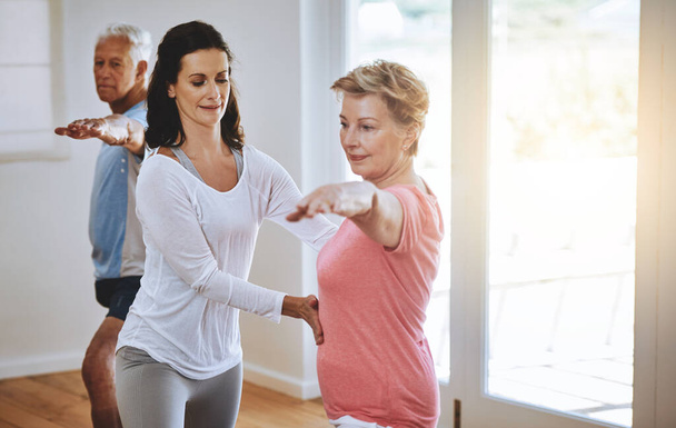 Vivir un estilo de vida saludable a través del yoga. un profesor ayudando a una mujer mayor durante una clase de yoga - Foto, imagen