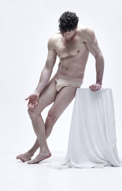 Портрет красивого чоловіка з м'язовим рельєфним тілом, який позує без сорочки в нижній білизні на білому фоні студії. Концепція естетики чоловічого тіла, чоловіча краса, натхнення, мистецтво
 - Фото, зображення