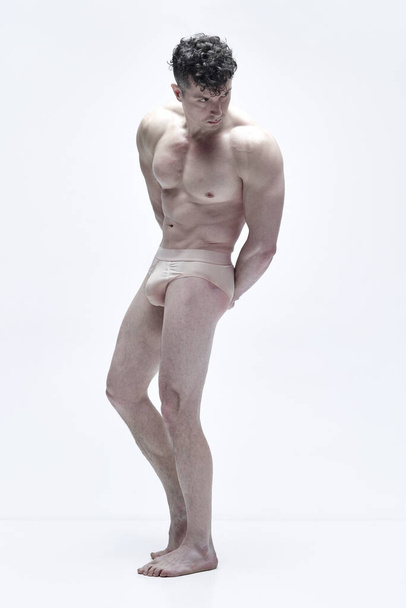 Full-length portrait of mature man with attractive, strong, muscular body posing shirtless in underwear against white studio background. Concept of male body aesthetics, mens beauty, inspiration, art - Valokuva, kuva
