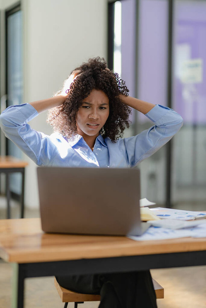 Mujer de negocios africana estresada y dolor de cabeza con papeleo cansado que sufre de dolor de cabeza temporal en el resumen del equipo Estrés en el lugar de trabajo o concepto de migraña. - Foto, imagen