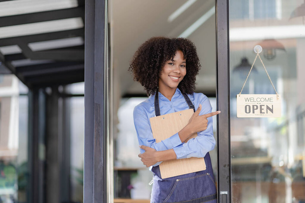 Barista Startup Coffee Shop Entrepreneur African American Woman Standing at the Door of a Casual Coffee Shop Showing an Open Sign Happy and cheerful smile with service, food and drink concept - Photo, image