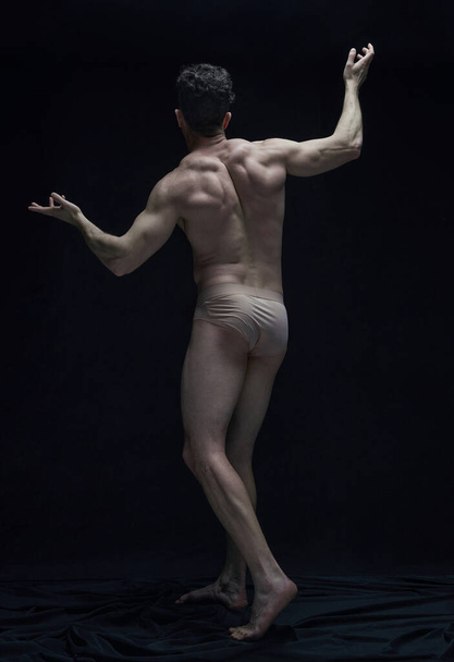 Full-length rear view portrait of handsome muscular shirtless man with relief strong body posing against black studio background. Concept of male body aesthetics, mens beauty, inspiration, art - Photo, Image