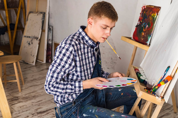 Thoughtful painter or artist In a denim overalls and checkered shirt working on a new art in a workshop. - 写真・画像
