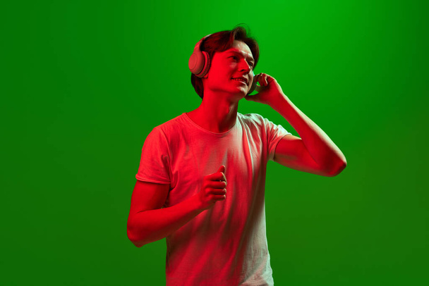 Ilo, hauskuus, suosikki. Banner yksi houkutteleva kaveri yllään kuulokkeet kuunnella musiikkia nauttia kasvot yli vihreä neon tausta. Käsite musiikki, harrastus, tunteet, mieliala, mainos - Valokuva, kuva